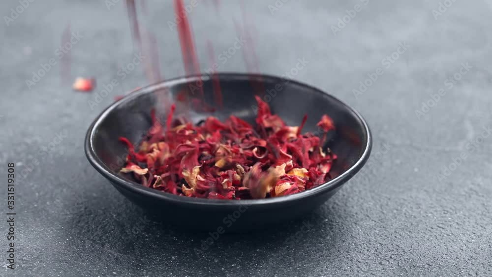 Hibiscus tea leaves falling down into a black bowl. Grey background. Close up. Hibiscus tea leaves falling down into a black bowl. Grey background. Close up.