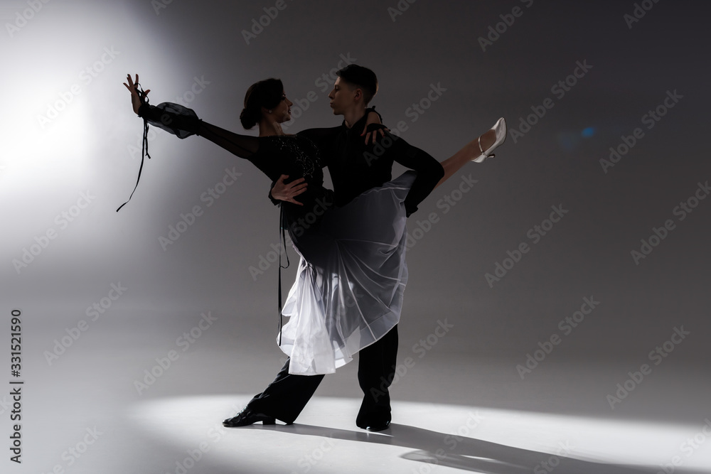elegant young couple of ballroom dancers in black outfit dancing in dark