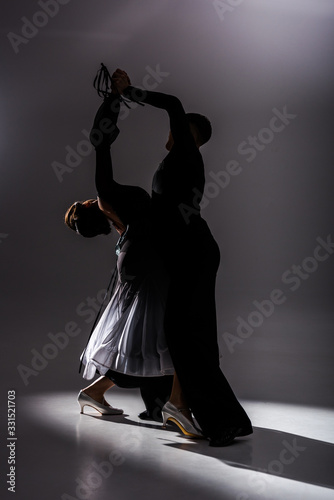 elegant young couple of ballroom dancers in black outfit dancing in dark