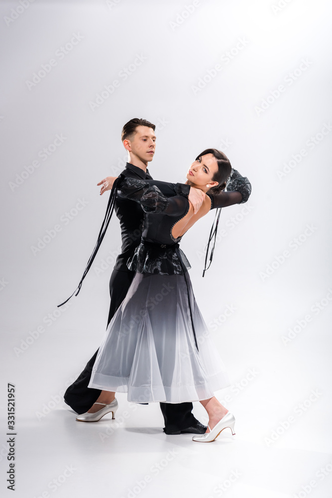 Fototapeta premium elegant young couple of ballroom dancers in black outfit dancing on white