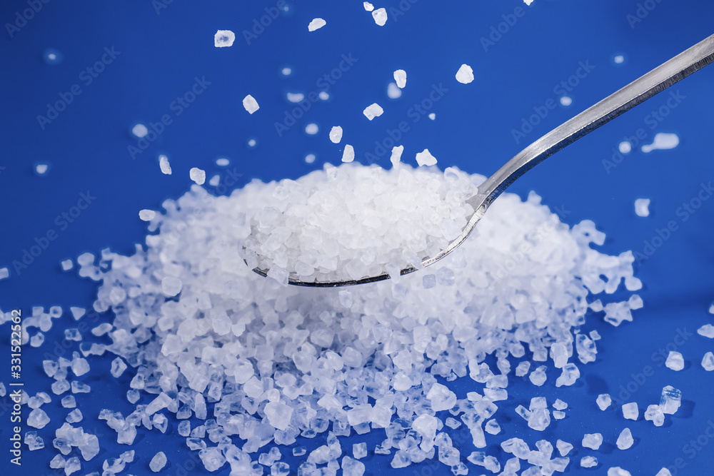 Coarse sea salt in a spoon. Some salt crystals pour on top Coarse sea salt in a spoon. Some salt crystals pour on top