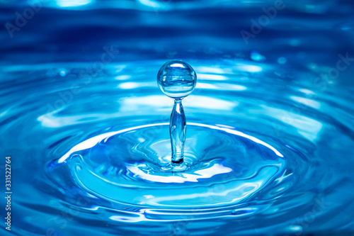 A drop of blue water falls into the water surface. Close-up. Splashes of water and concentric circles.
