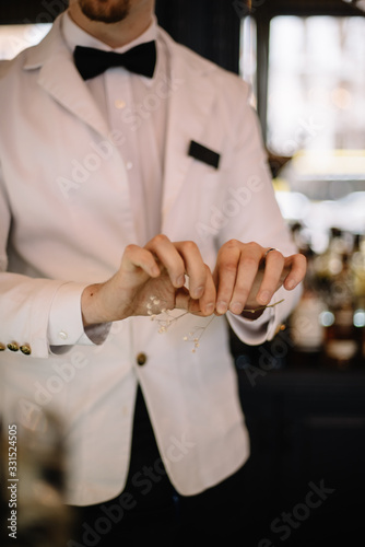 Bartender in a white suite and black bow tie prepare decorating for a cocktail with dried flower branch. Smooth image with shallow depth of field.