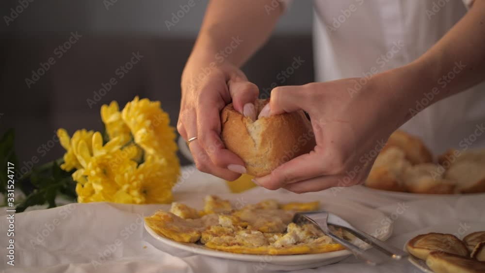 A young woman is having breakfast of scrambled eggs with bun and breaking it apart in slow motion. A young woman is having breakfast of scrambled eggs with bun and breaking it apart in slow motion.