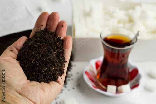 Some dry black tea in hand in front of traditional Turkish Tea.