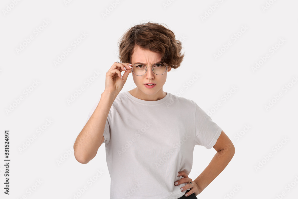 Suspicous young woman holding eyeglasses with one hand examining what she sees. Suspicous young woman holding eyeglasses with one hand examining what she sees.