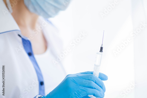Female doctor or nurse in medical mask holding syringe with injection