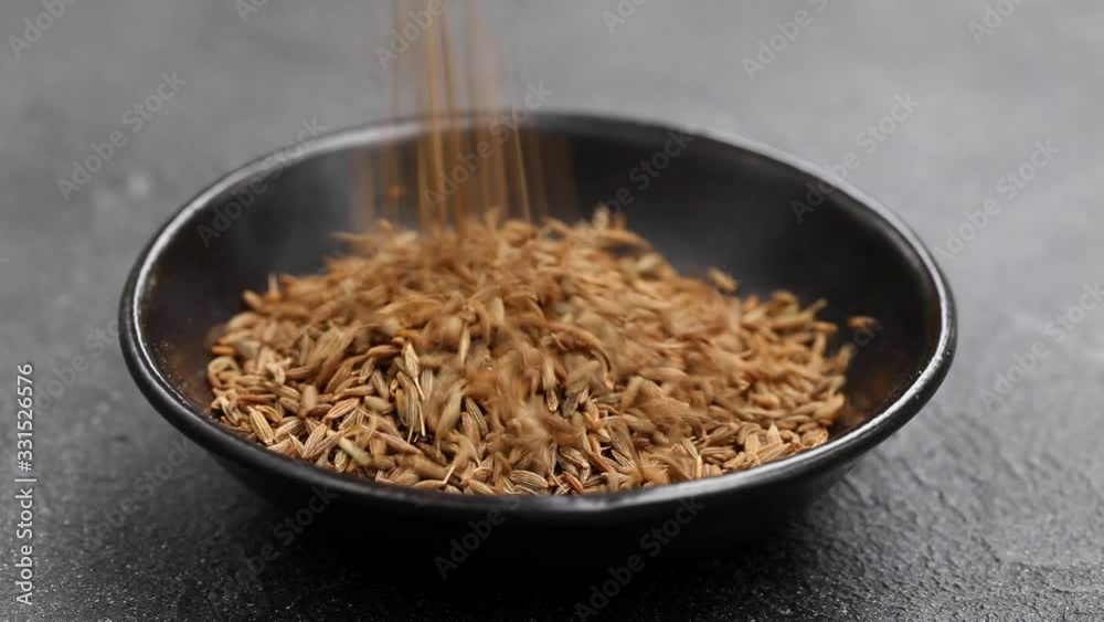Cumin seeds falling down to a black bowl. Dark background. Close up. Cumin seeds falling down to a black bowl. Dark background. Close up.