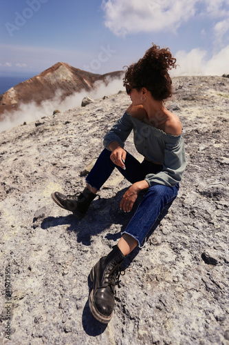 I love mountains. Young female blogger in casual clothes sitting on the top of mountain and looking away. Woman traveler enjoying wonderful nature