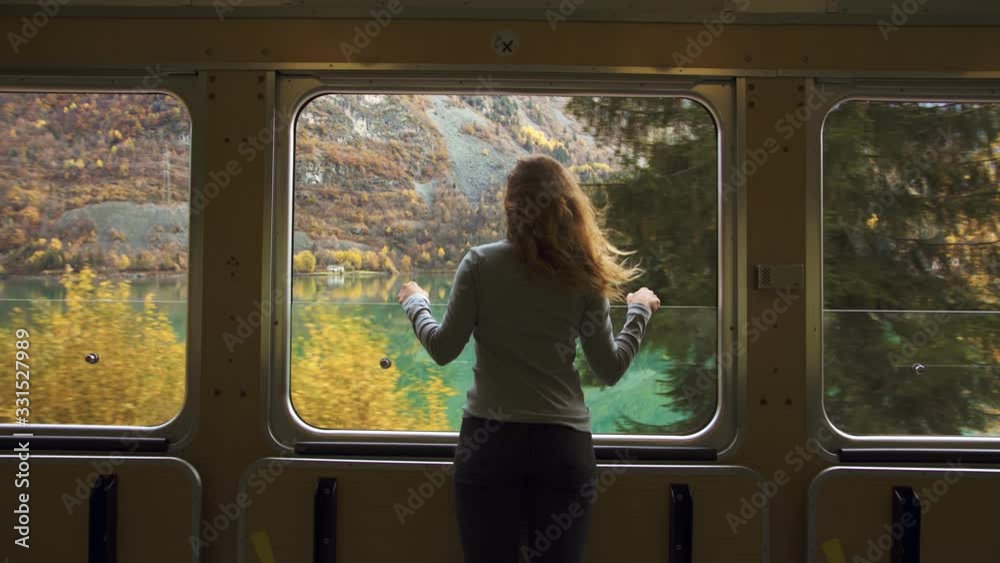 Cinematic and symmetric beautiful shot of young travelling woman, adventurer and female nomad look out of open window of tourist train in swiss mountains. Travel inspiration and wanderlust dreams