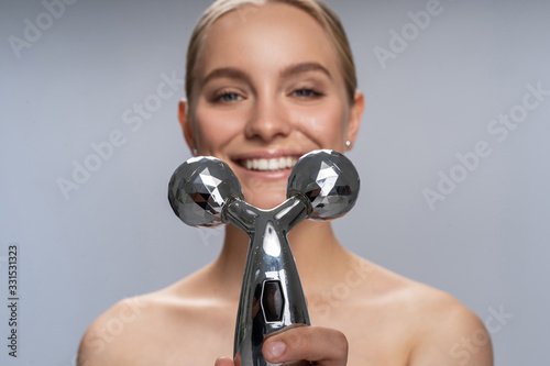 Cheerful blonde woman showing her face massager