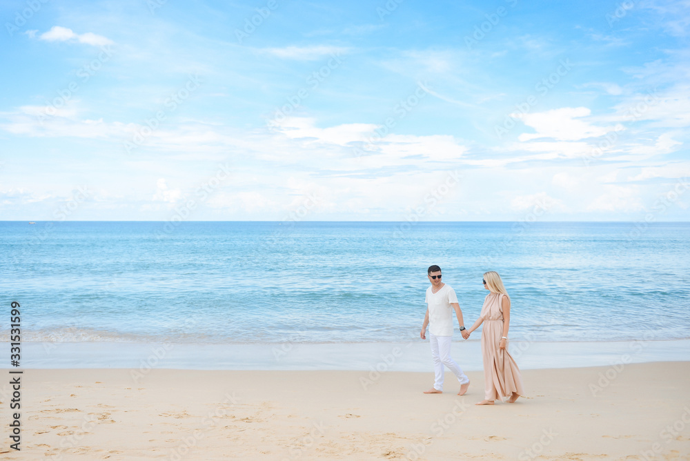Young attractive man and woman in love walk and hug against the background of white sand and azure sea. Travel, honeymoon Young attractive man and woman in love walk and hug against the background of white sand and azure sea. Travel, honeymoon