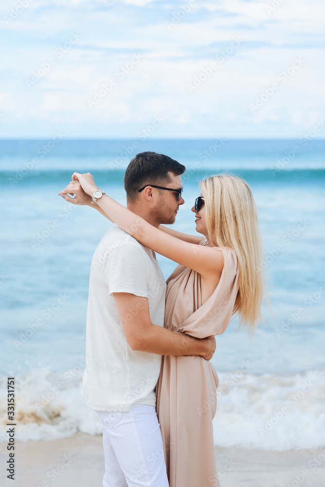 Young attractive man and woman in love walk and hug against the background of white sand and azure sea. Travel, honeymoon Young attractive man and woman in love walk and hug against the background of white sand and azure sea. Travel, honeymoon