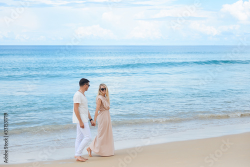 Young attractive man and woman in love walk and hug against the background of white sand and azure sea. Travel, honeymoon