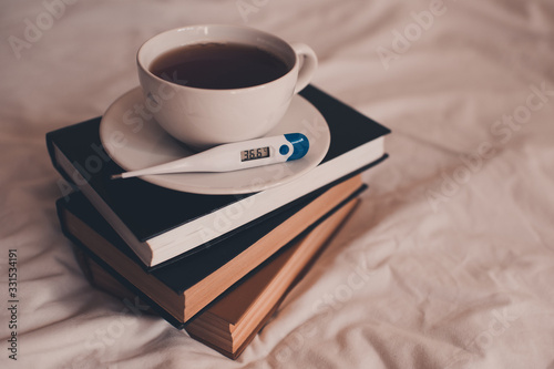 Cup of tea with thermometer with normal temperature on stack of book closeup. Good morning. Virus concept.
