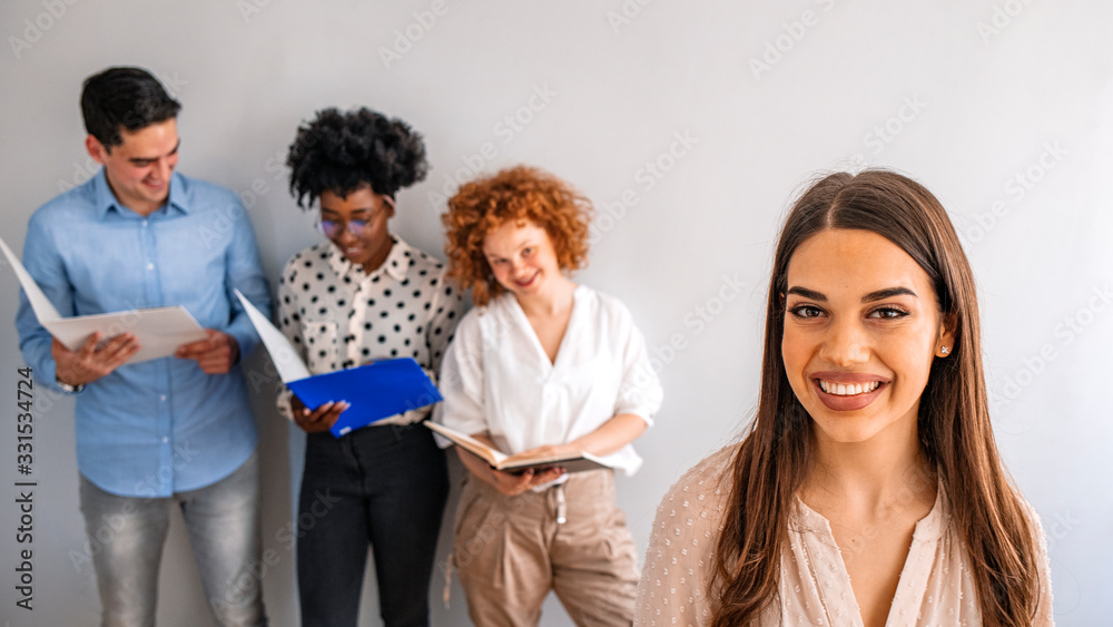 Portrait of a young creative standing in an office with colleagues in the background. Portrait of a young designer standing in an office with her colleagues in the background Portrait of a young creative standing in an office with colleagues in the background. Portrait of a young designer standing in an office with her colleagues in the background