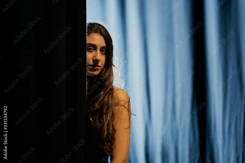 A woman shows half of her body behind the backdrop of a stage in a dark environment A woman shows half of her body behind the backdrop of a stage in a dark environment