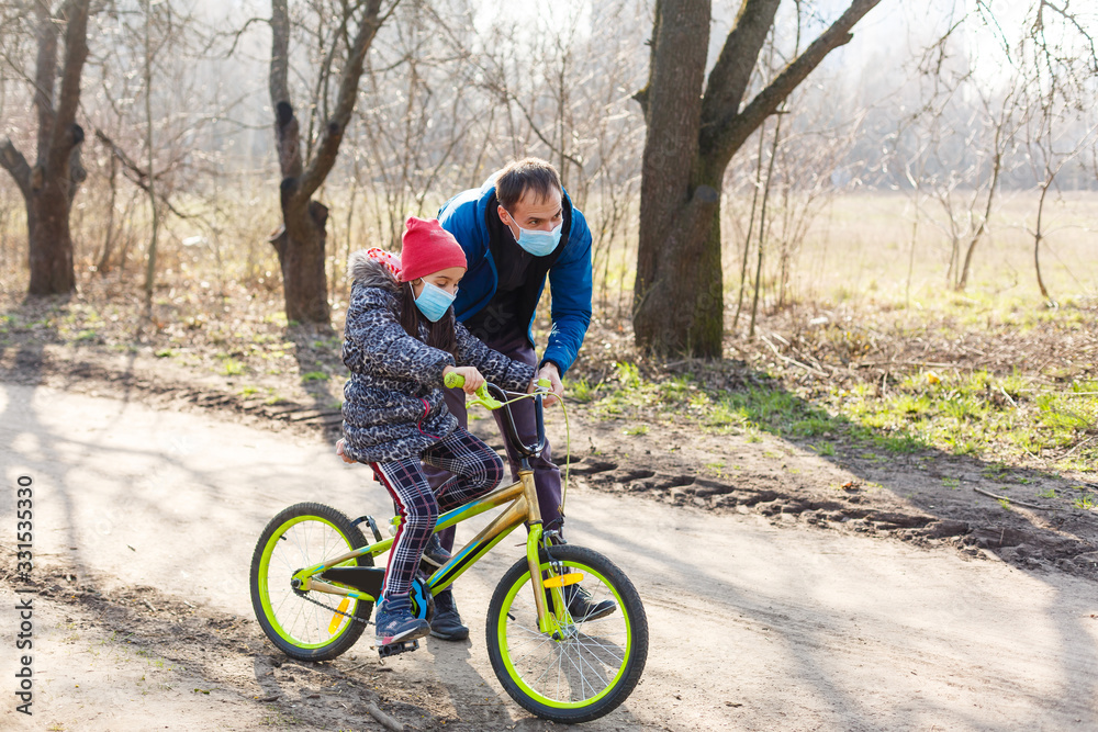 Little girl wearing medical mask prevent flu, pollutions and covid-19 riding bicycle outdoor. Little girl wearing medical mask prevent flu, pollutions and covid-19 riding bicycle outdoor.