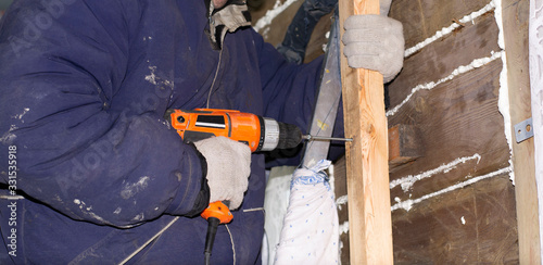 the worker fastens the wooden rail with an electric screwdriver to the wall.