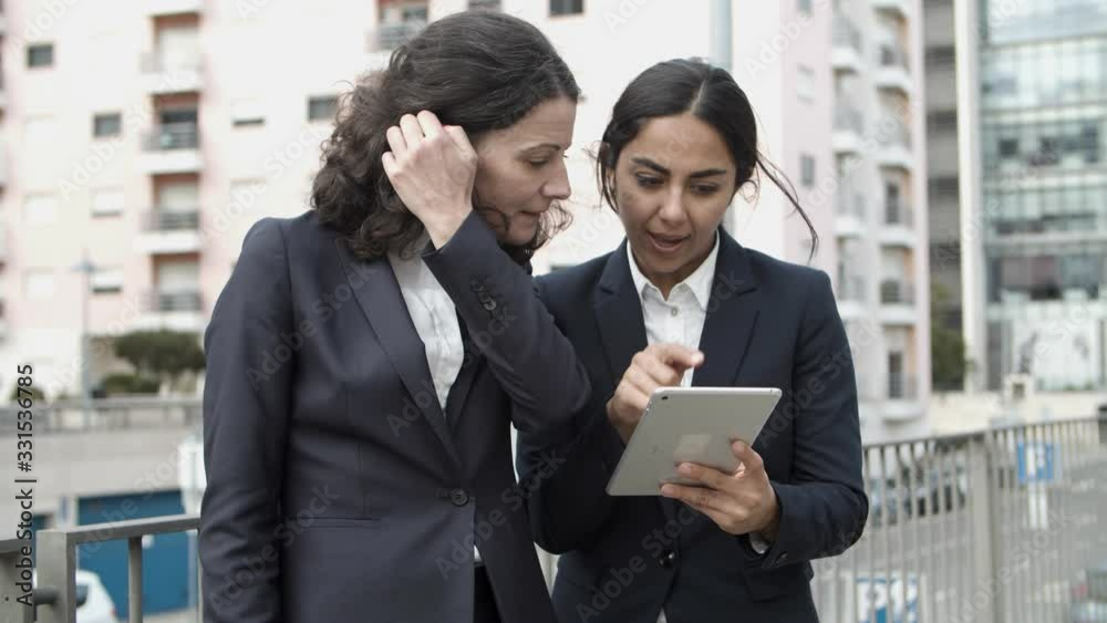 Businesswomen using tablet pc on street. Focused female colleagues using digital tablet and discussing work outdoors. Business and technology concept Businesswomen using tablet pc on street. Focused female colleagues using digital tablet and discussing work outdoors. Business and technology concept