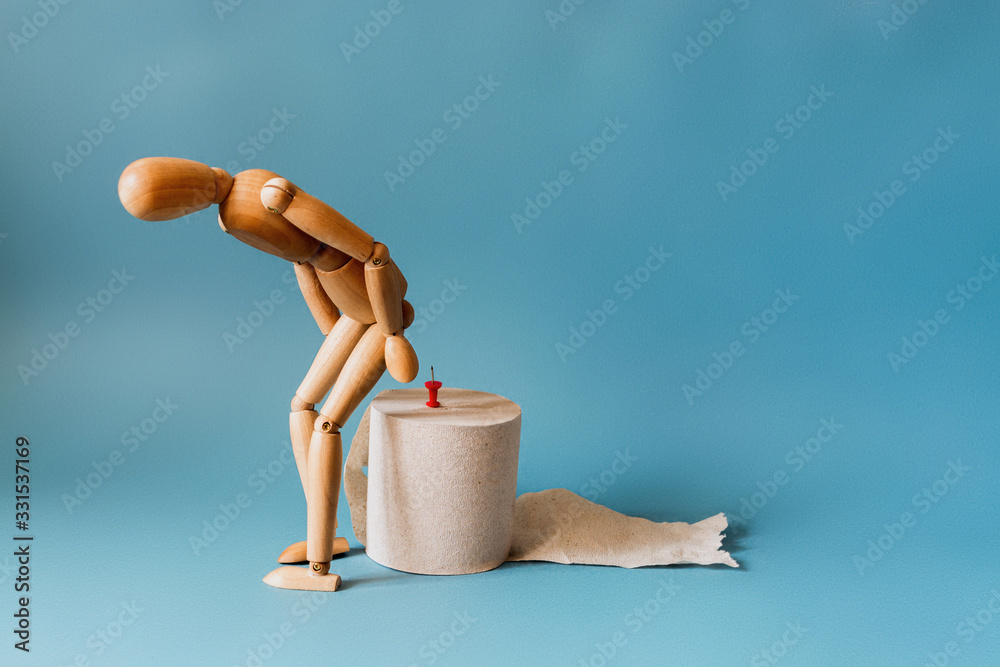 Wooden figure sit on a roll of toilet paper. Concept of the problem with hemorrhoids.