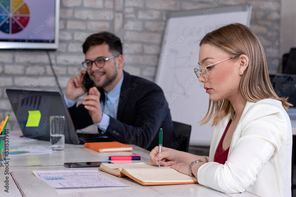 Business manager talking on cell phone and a beautiful young secretary or businesswoman, working together in a modern retro style office. Startup concept. Business manager talking on cell phone and a beautiful young secretary or businesswoman, working together in a modern retro style office. Startup concept.