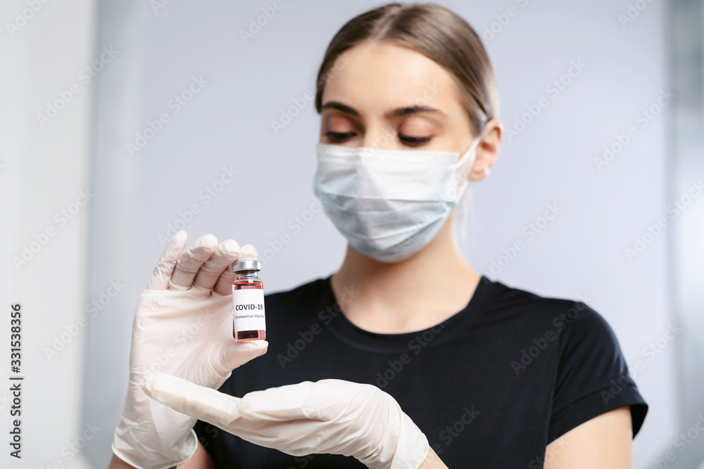 Bottle of corona virus COVID-19 vaccine in hand of woman patient in disposable facial mask. Coronavirus 2019-nCoV concept.
