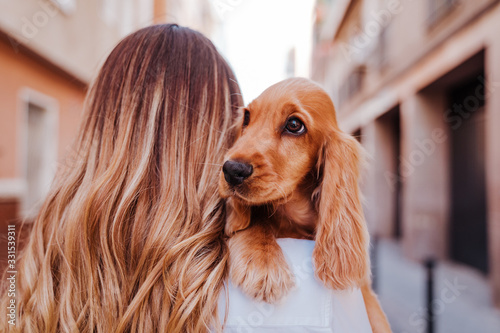 young woman at the street holding with her cute cocker dog on shoulder. Lifestyle outdoors with pets