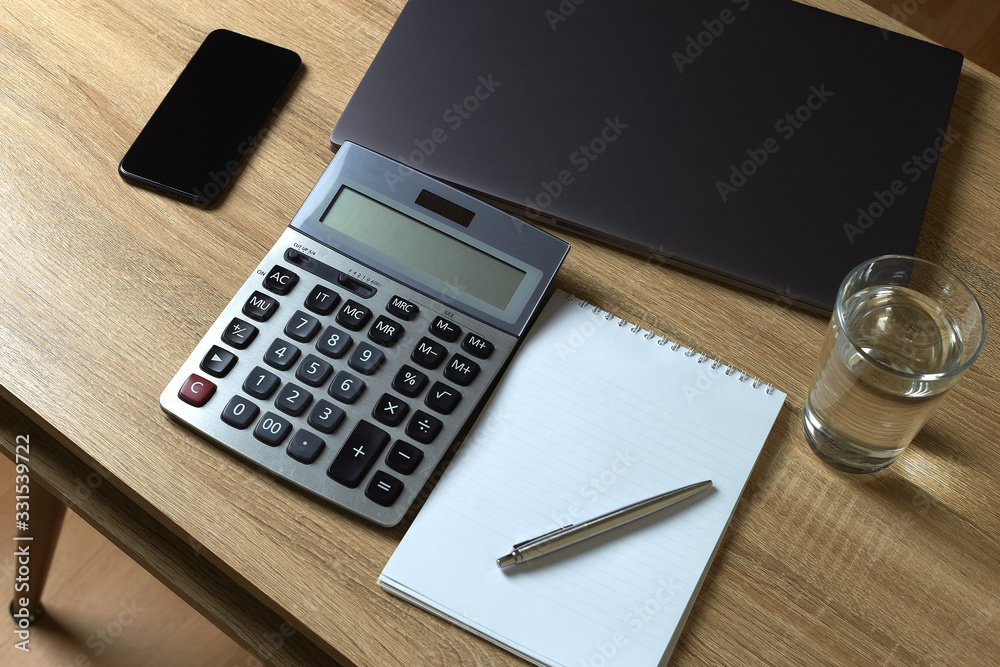 Remote work laptop calculator phone notepad with pen and glass of water on the table Remote work laptop calculator phone notepad with pen and glass of water on the table