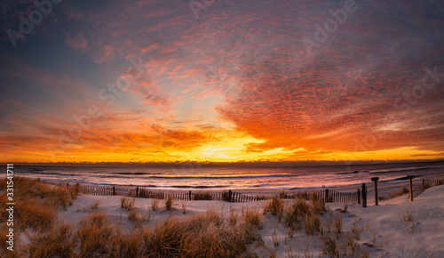 Panoramic sunrise at the beach with a dune fence in the foreground