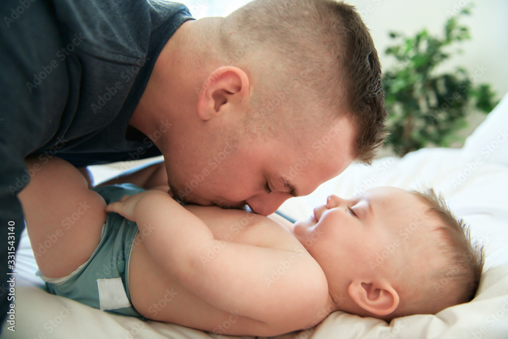 young father is laying down on a bed and holding is baby. young father is laying down on a bed and holding is baby.
