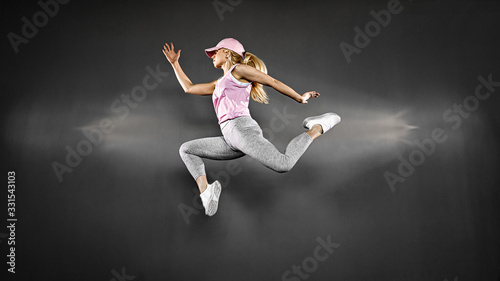 Young blonde woman with fit body jumping and running against grey background. Female model in sportswear exercising.