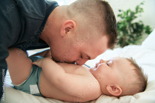young father is laying down on a bed and holding is baby.