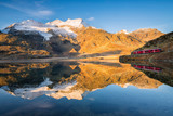  The Swiss train reflected in the white lake in the background the peaks of the Alps, Bernina Pass, Switzerland