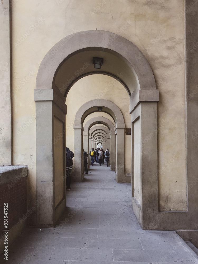 a sidewalk full of architectural arches with people walking on the distance