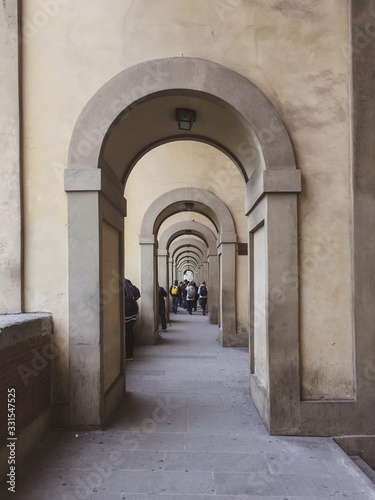 a sidewalk full of architectural arches with people walking on the distance
