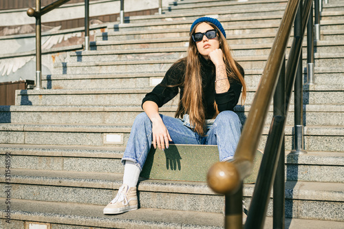 Young caucasian woman posing on street with skateboard in hands. Teenager girl in blue jeans extreme sports in an urban environment. Theme of youth recreation, lifestyle. Skateboarder in the city photo