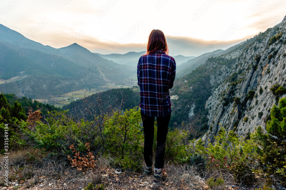 A full body shot of a young female hiker / adventurer in the French Alps mountains during sunset posing and admiring the view
