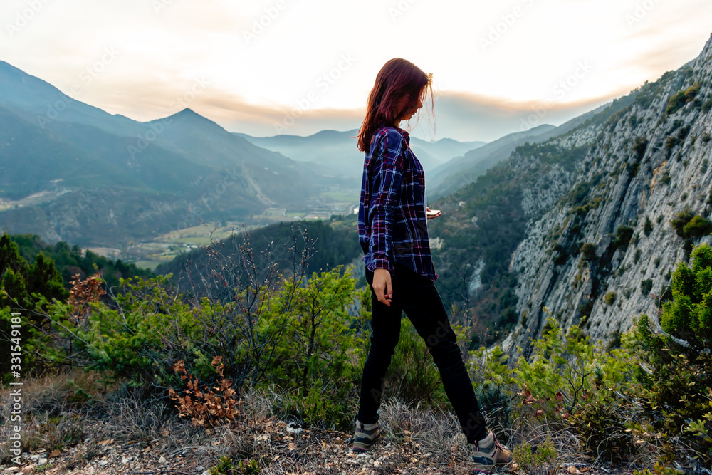 Fototapeta premium A full body shot of a young female hiker / adventurer in the French Alps mountains posing during sunset