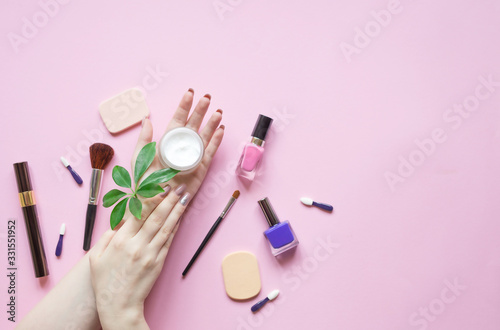 Natural Cosmetics for skin care and makeup accessories. Beautiful woman's hands holding cream and green plant on pastel pink background. 