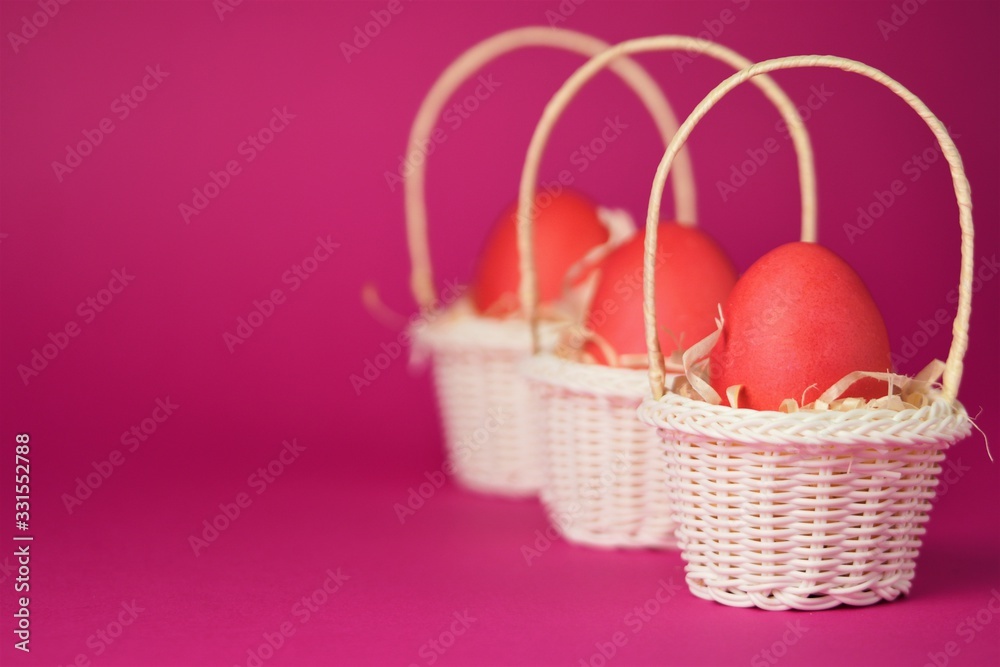 Pink chicken eggs in a white wicker basket covered with straw a bright pink background. Holiday card with space for text.Easter symbol.Copy space.