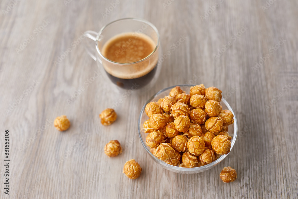 Appetizing caramelized popcorn and cup of coffee. Heap of homemade delicious popcorn on a wooden background. Snacks and food for a movie theater or cinema. Fastfood background. Appetizing caramelized popcorn and cup of coffee. Heap of homemade delicious popcorn on a wooden background. Snacks and food for a movie theater or cinema. Fastfood background.