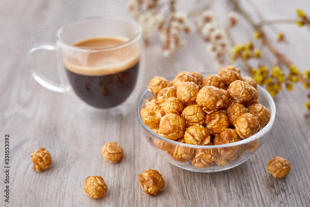 Appetizing caramelized popcorn and cup of coffee. Heap of homemade delicious popcorn on a wooden background. Snacks and food for a movie theater or cinema. Fastfood background. Appetizing caramelized popcorn and cup of coffee. Heap of homemade delicious popcorn on a wooden background. Snacks and food for a movie theater or cinema. Fastfood background.