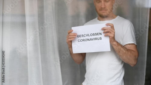 Man showing card in window with information closed due to coronavirus in German language. Business closed during coronavirus epidemic.