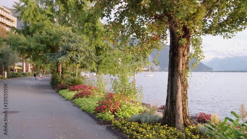 Flow shot magic hour time fromt Swiss promenade to Lake Geneva at Montreux through trees. Unrecognized tourists making photos
