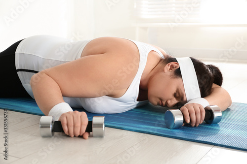 Canvas Print Lazy overweight woman with dumbbells sleeping on mat instead of training at gym