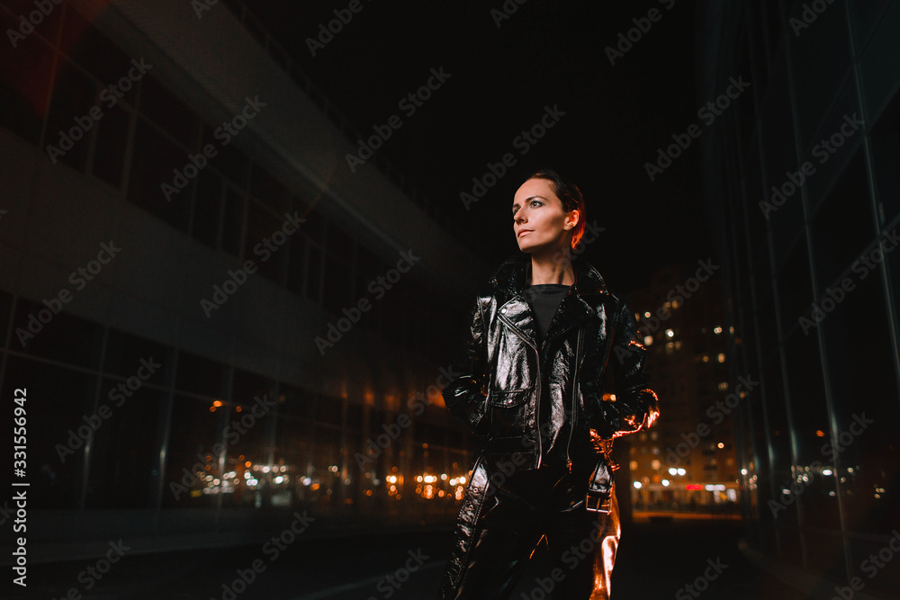 Naklejka premium Portrait of a girl on the street of a night city in leather clothes in the light of lanterns