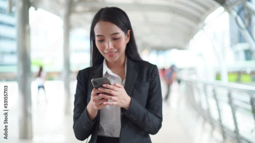 Young beautiful Asian woman reading a good news from mobile phone and dancing victory dance in the business district