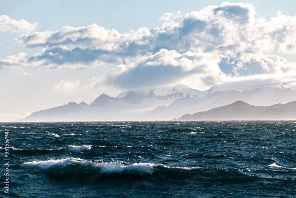 Wellen auf dem Meer in der Antarktis mit der Küste im Hintergrund, Wolken und Eis der Gletscher 