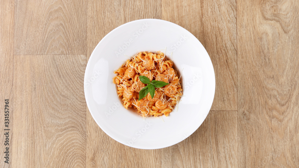 Fusilli with Shrimp pasta with basil leaves and Parmesan cheese in a white plate on a wooden background